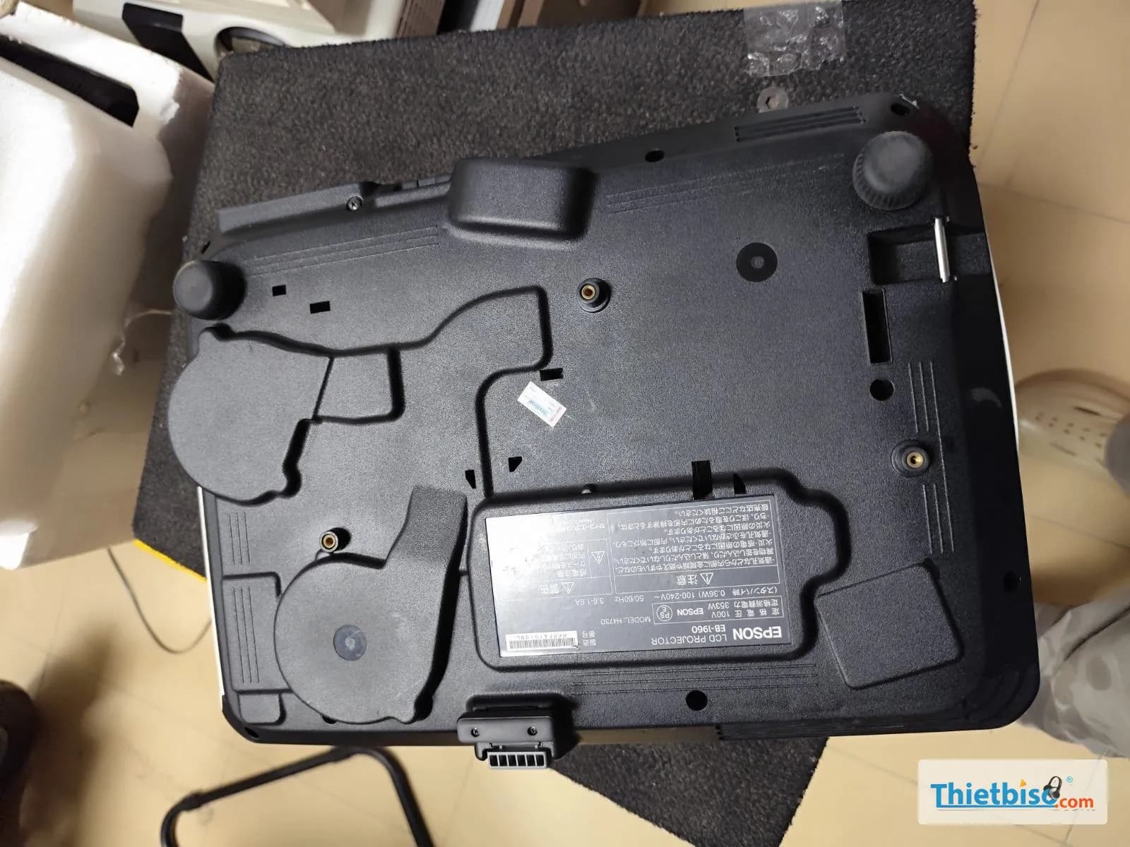 Mặt đáy máy chiếu Epson EB-1960 đặt trên thảm đen, thấy nhãn model