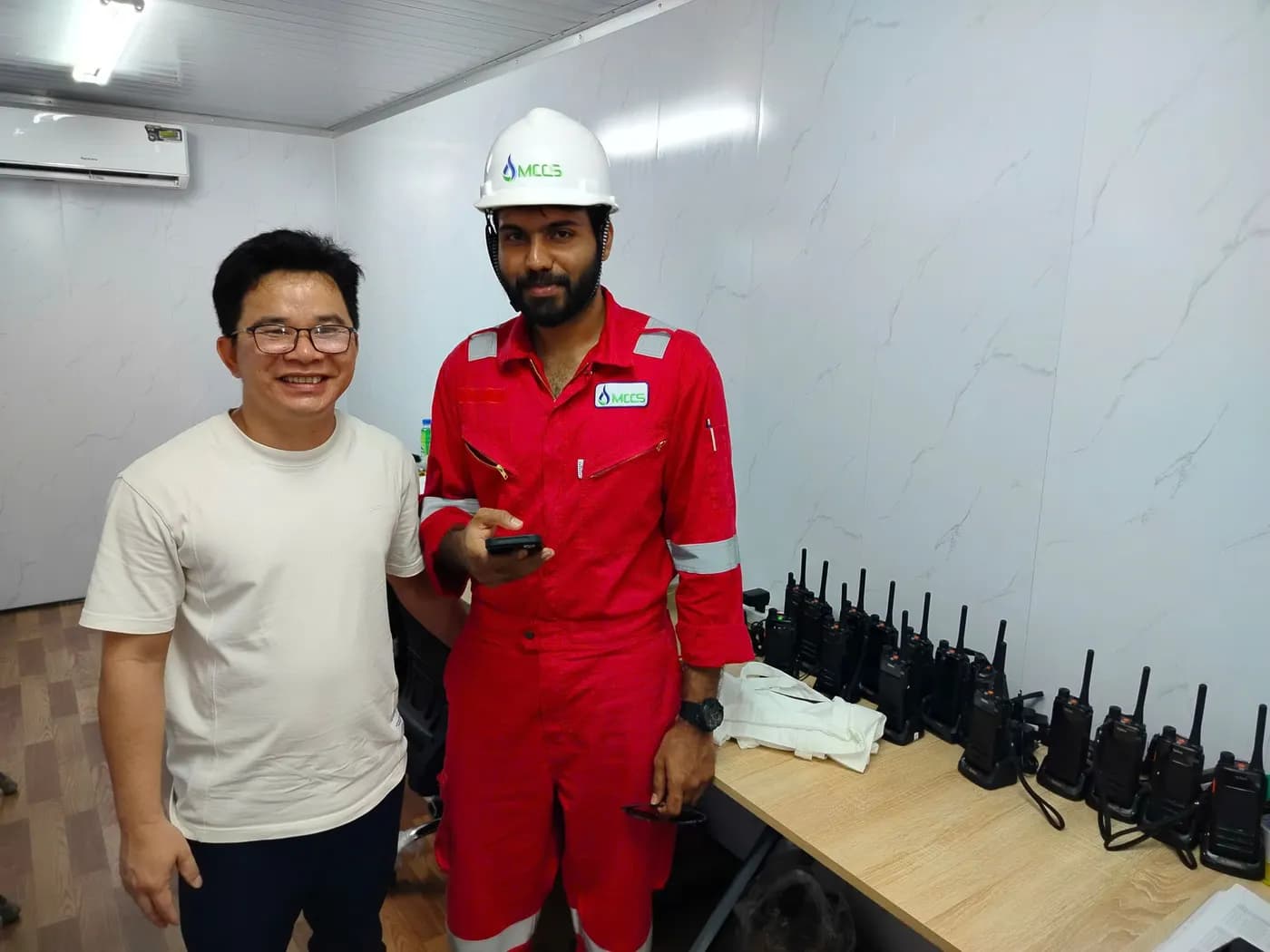 Nhân sự đội mũ, mặc áo logo MCCS cạnh dãy bộ đàm Hytera