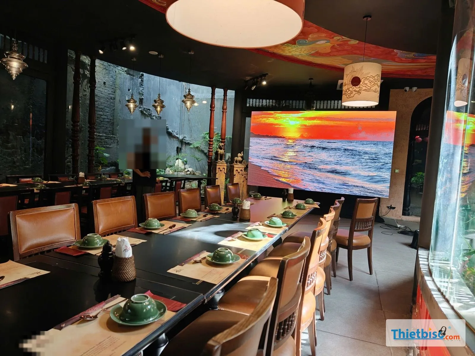 Màn LED hiển thị cảnh hoàng hôn trên biển trong nhà hàng, bàn tiệc dài phía trước