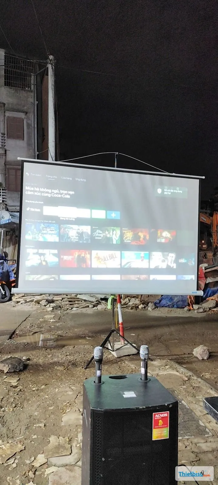 Màn chiếu chân và loa kéo kèm hai micro đặt ngoài trời ban đêm