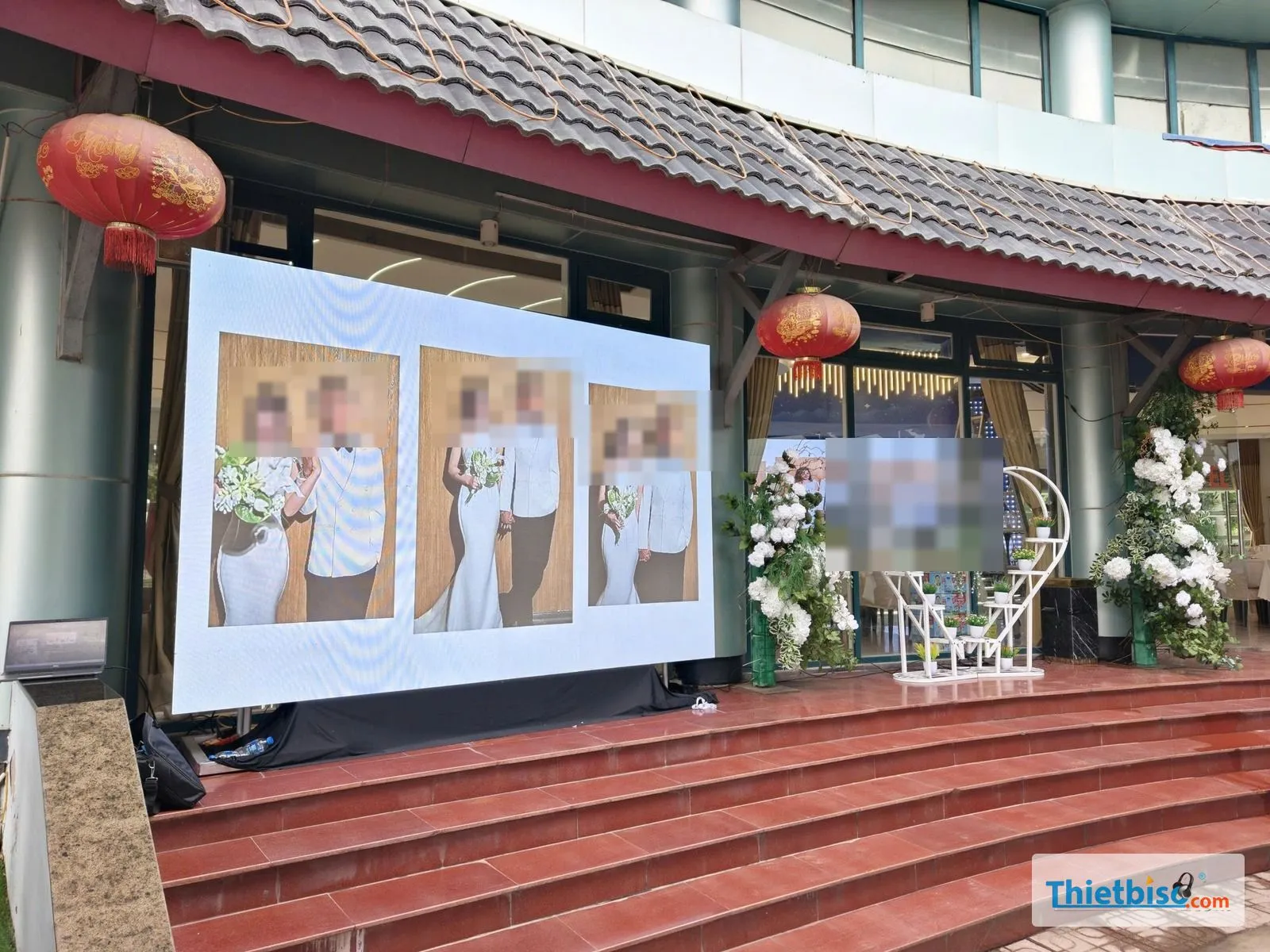 Màn LED lớn ngoài trời trước sảnh tiệc cưới hiển thị ảnh cưới, bên cạnh có hoa trang trí