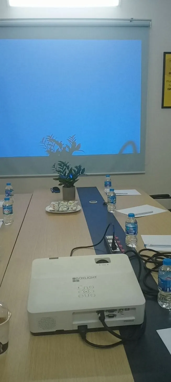 Máy chiếu đặt trên bàn họp dài, phía sau là màn chiếu treo tường
