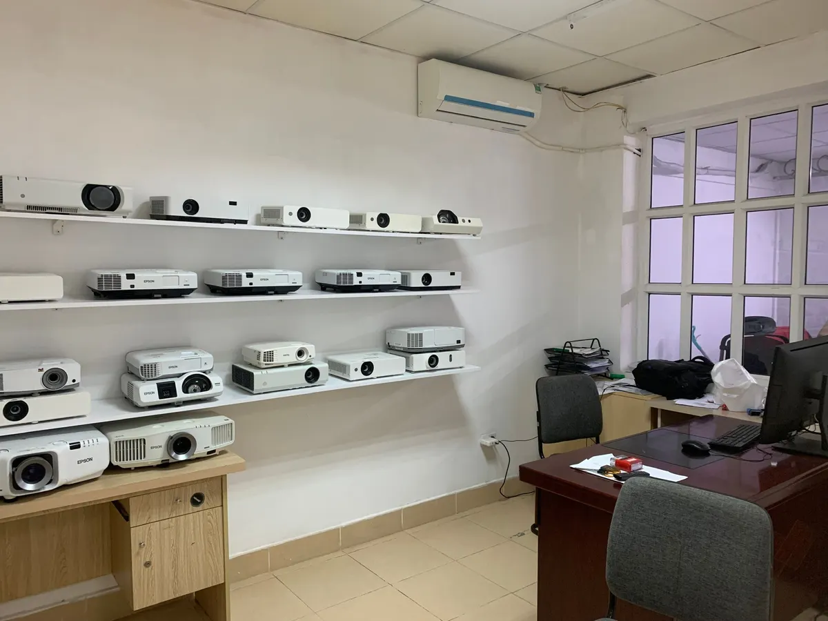Kệ trắng xếp các máy chiếu cho thuê, bàn làm việc đặt gần cửa sổ