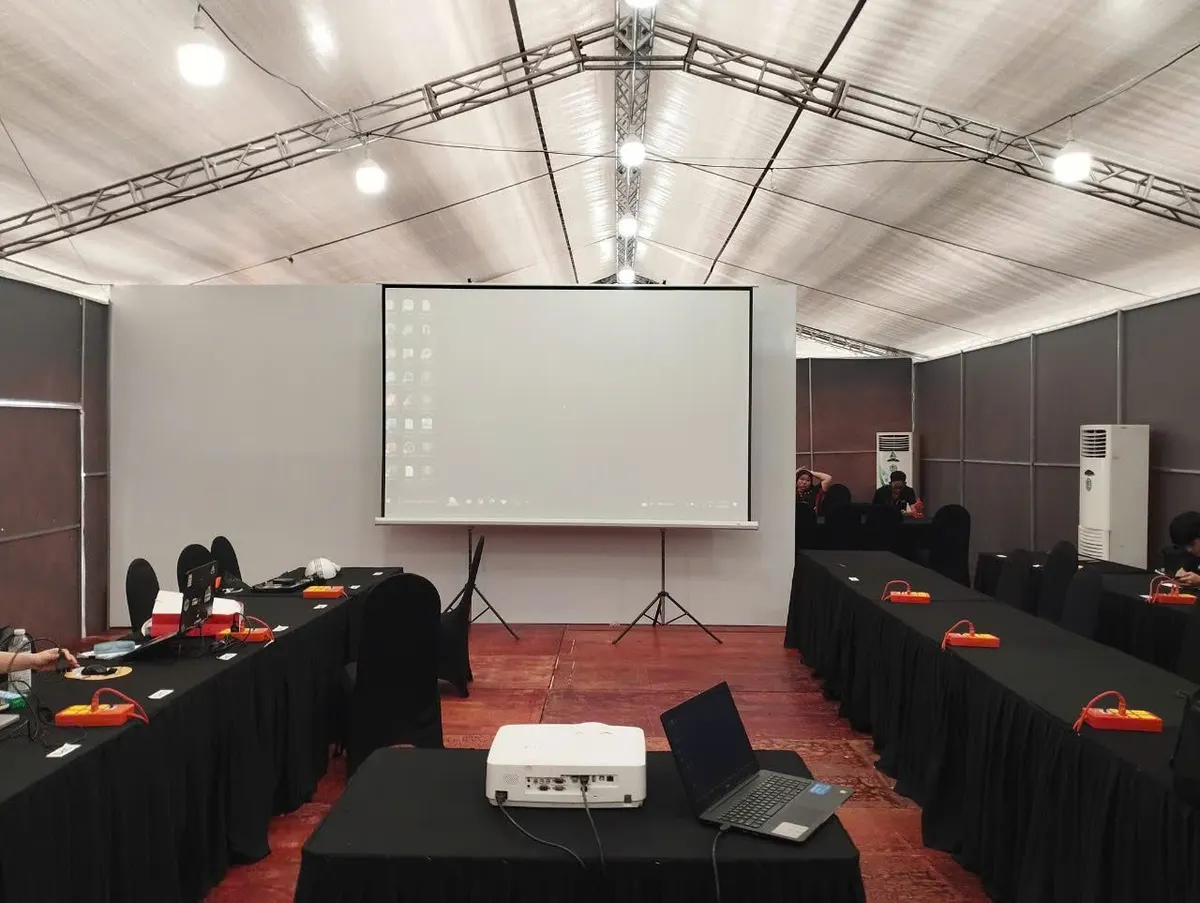 Hội nghị trong nhà bạt có màn chiếu chân, máy chiếu và laptop đặt trên bàn phủ khăn đen